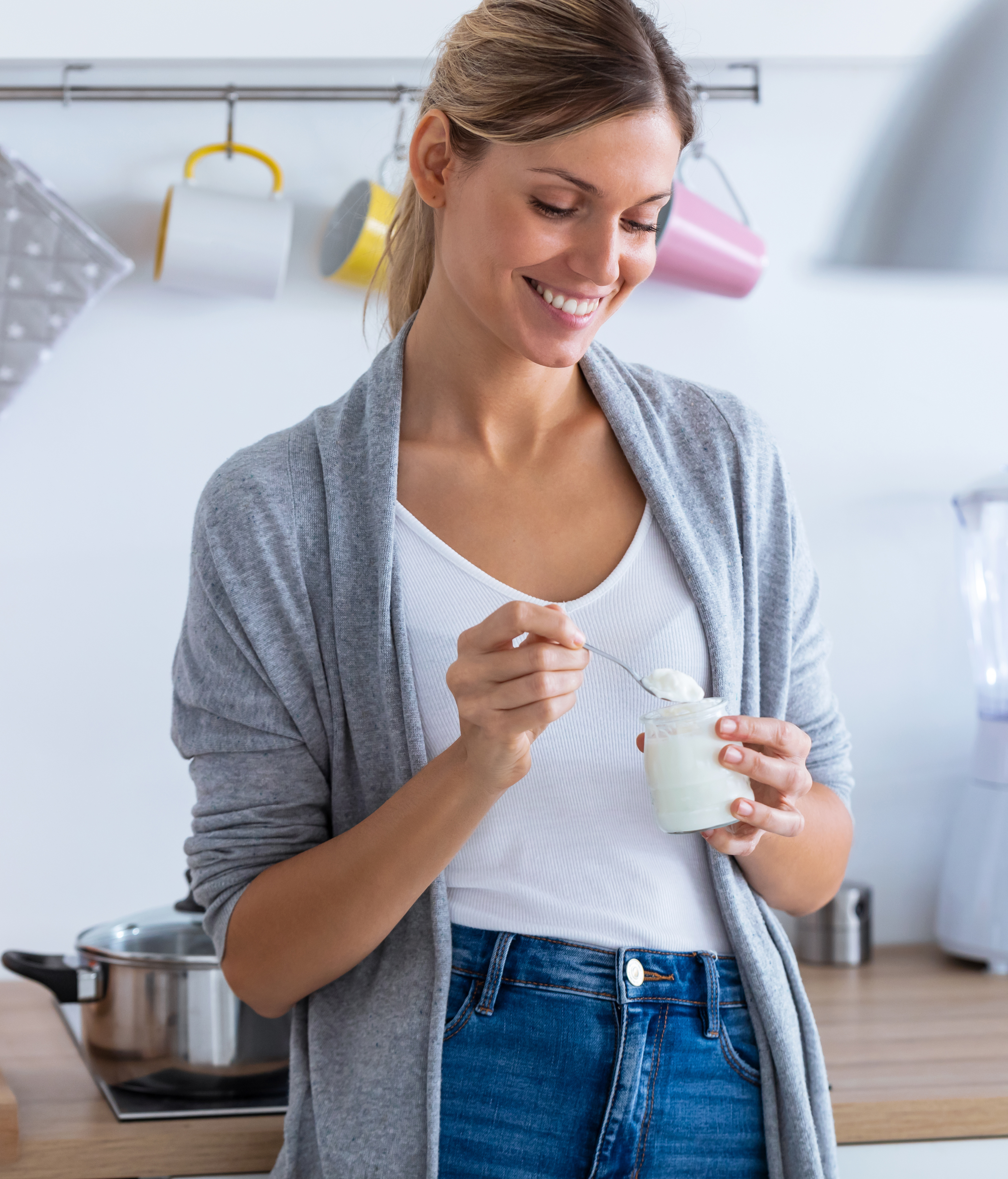 Shot of pretty young woman eating yogurt while standing in the kitchen at home.